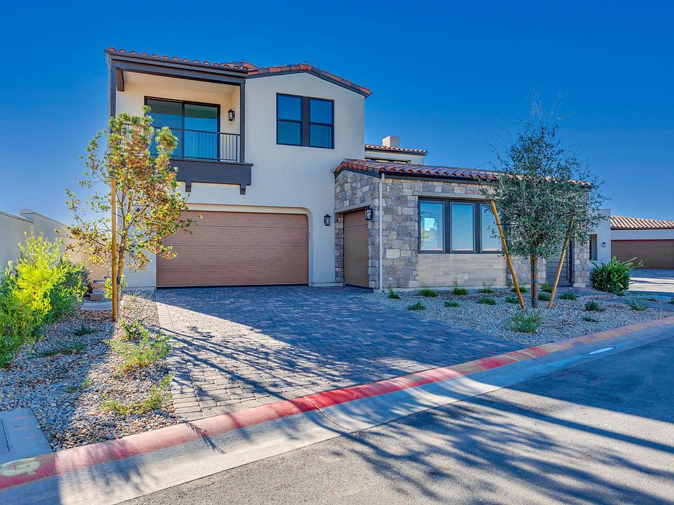 A modern two-story house with a stone exterior, surrounded by landscaping and a paved driveway, set