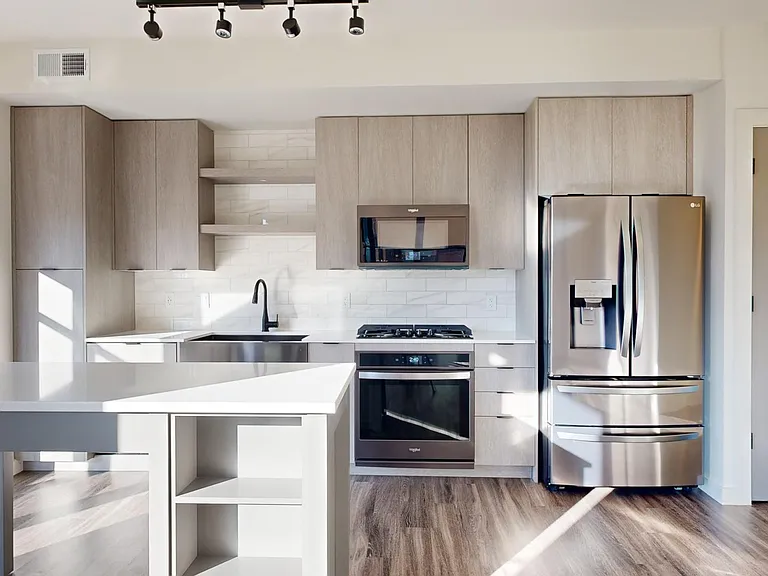 Apartment kitchen with black stainless steel appliances, quartz countertops, wood-style flooring, and custom Italian cabinetry.