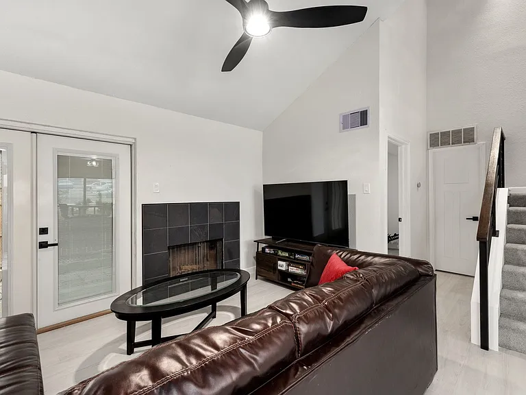 Living room featuring high vaulted ceiling, french doors, ceiling fan, light hardwood / wood-style floors, and a tiled fireplace