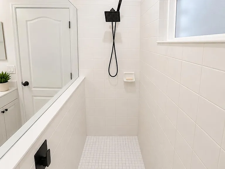 Walk-in tiled shower with rainfall-style fixture, built-in soap dish, and a frosted window for privacy and light.