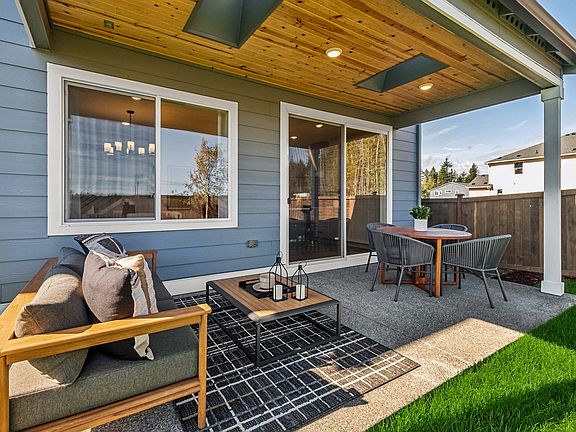 A cozy outdoor patio with a wooden ceiling, comfortable seating, and a grassy area, surrounded by a