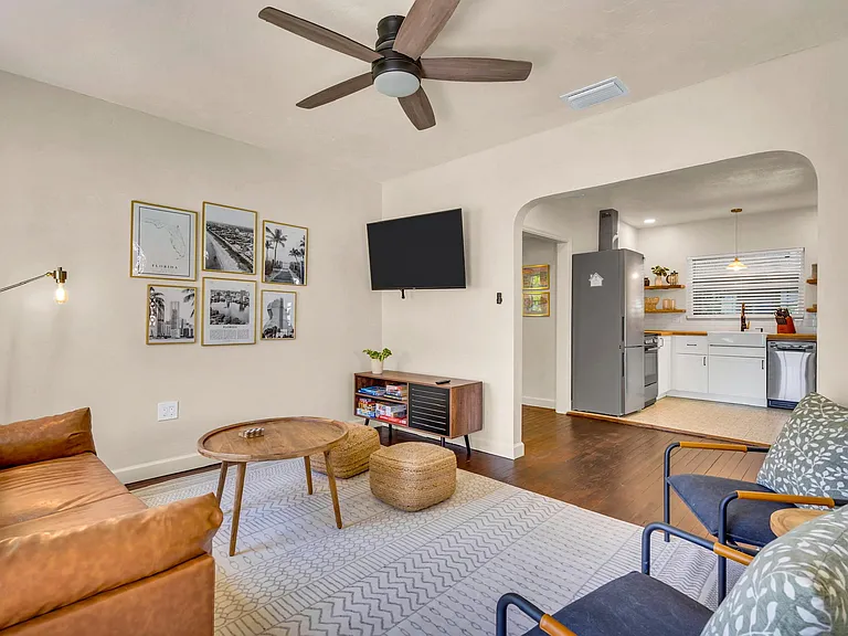 Open living area with seating, ceiling fan, and a TV wall, flowing into the adjacent kitchen for easy entertaining.