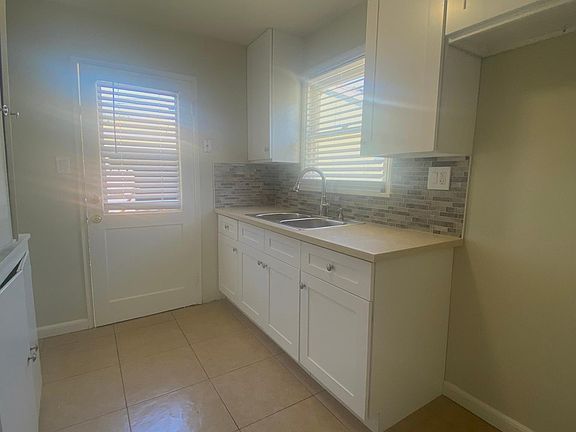 Updated kitchen cabinetry, counter, backsplash, and stainless-steel double sink with gooseneck sprayer faucet.