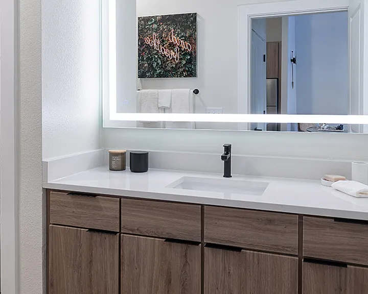 Apartment bathroom with wood-style flooring and LED vanity mirror.