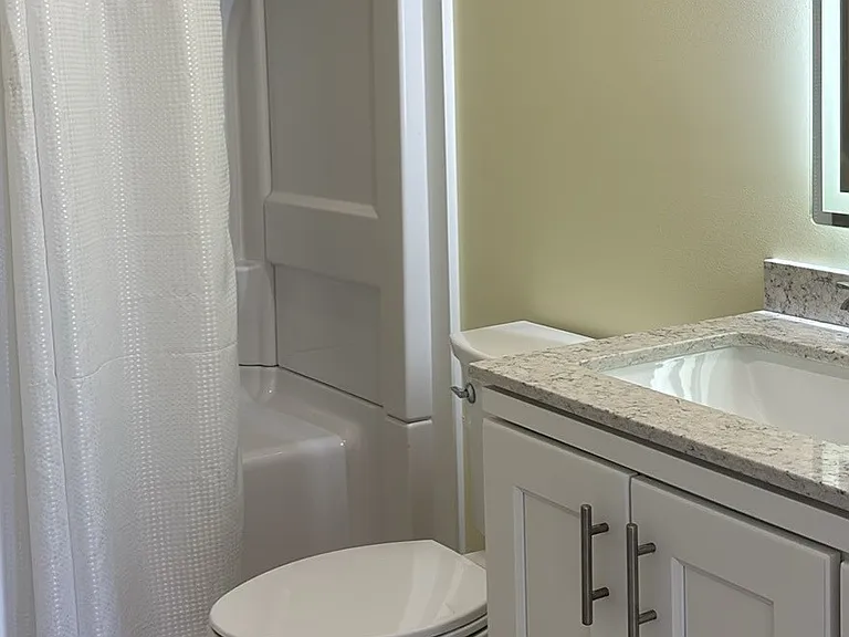 bathroom has large shower with seat and backlit mirror over vanity with storage.