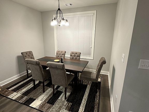 Dedicated dining area with a chandelier, large window with blinds, and space for a full table and seating.