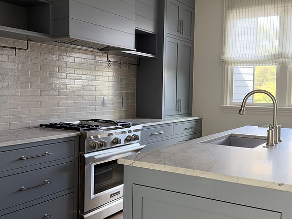 Kitchen with custom cabinets and hardware, pot racks, utensil drawers, double trash pullout, range and dishwasher.