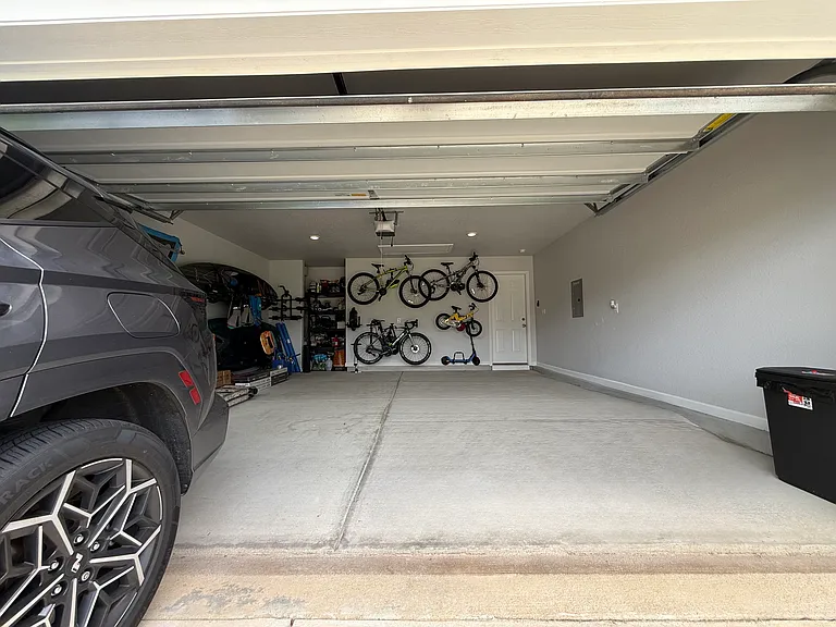 Two-car garage with finished walls and ceiling; racks for hanging four bicycles, two electric scooters, a bike trailer, and a jogging stroller; space for lawn mowers; and shelving to organize tools and other items.