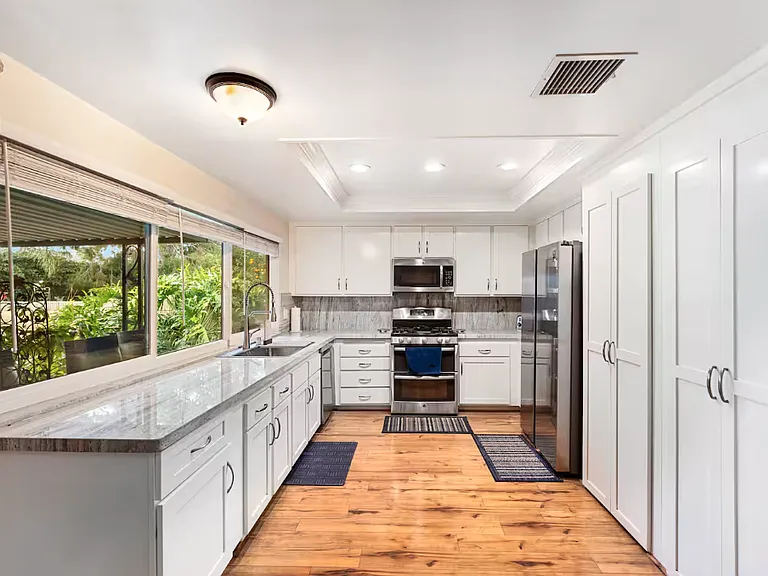 This is the view of the kitchen from the family/TV room. It has lots of cupboards plus a pantry. It has the refrigerator, microwave and stove. It has waterproof wooden floors.