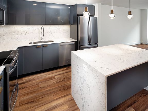 Renovated Package I kitchen with grey cabinetry, white marbled quartz countertops and backsplash, stainless steel appliances, and hard surface flooring (representative photo)