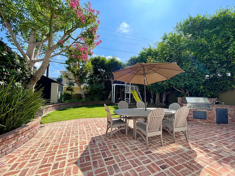 Family-friendly backyard featuring an outdoor dining table with umbrella, a children's play structure, and a large 8x12-foot storage shed_perfect for both entertaining and everyday play.
