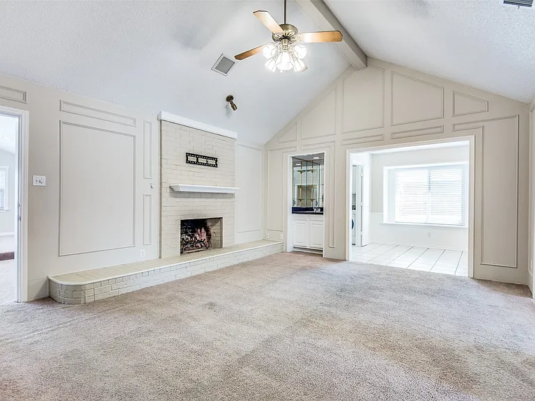 Vaulted ceiling living area featuring a brick fireplace, built-in wet bar, paneling details, and a ceiling fan