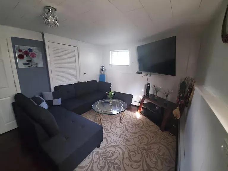 Comfortable living room with sectional seating, wall-mounted TV, and coffee table, plus a window for natural light.