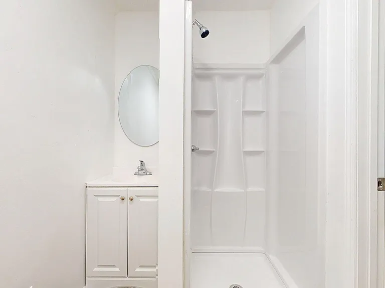 Clean private bath with walk-in shower, built-in shelving, vanity storage, and mirror.