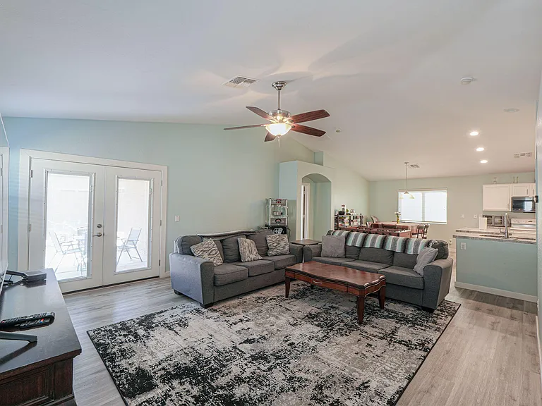 Open-concept living area with large sectional seating, ceiling fan, and French doors leading to the patio.