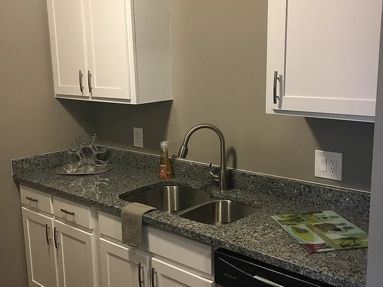 Updated kitchen with hardwood like flooring, white cabinets, granite grey countertops, a stainless steel sink, and stainless dishwasher.