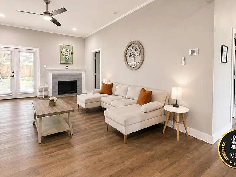 Spacious living room with a sectional, fireplace, and French doors to the yard, plus ceiling fan and durable flooring.