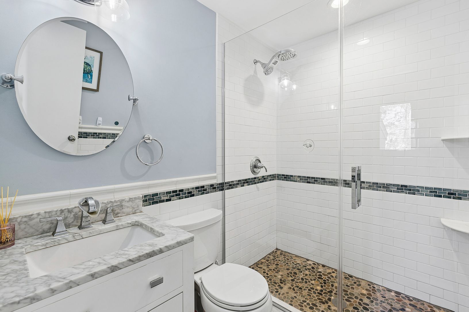 Full bathroom with stone-tiled shower floor and a decorative band of blue, black, and turquoise tile