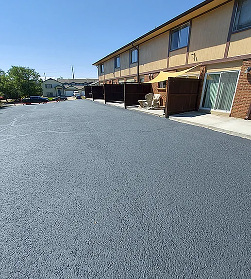 Bright and inviting apartment complex featuring spacious parking area and private outdoor seating, perfect for a sunlit relaxation spot.