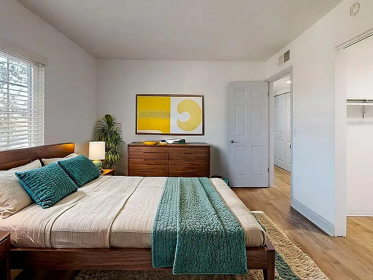 Inviting bedroom with modern decor, featuring a cozy wooden bed, vibrant teal accents, and a large closet. Sunlit space offers a serene and stylish retreat.