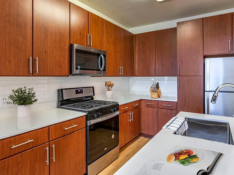 Newly renovated apartment homes feature kitchens with cherry cabinetry, white quartz countertops, stainless steel appliances, white tile backsplash, and hard surface flooring
