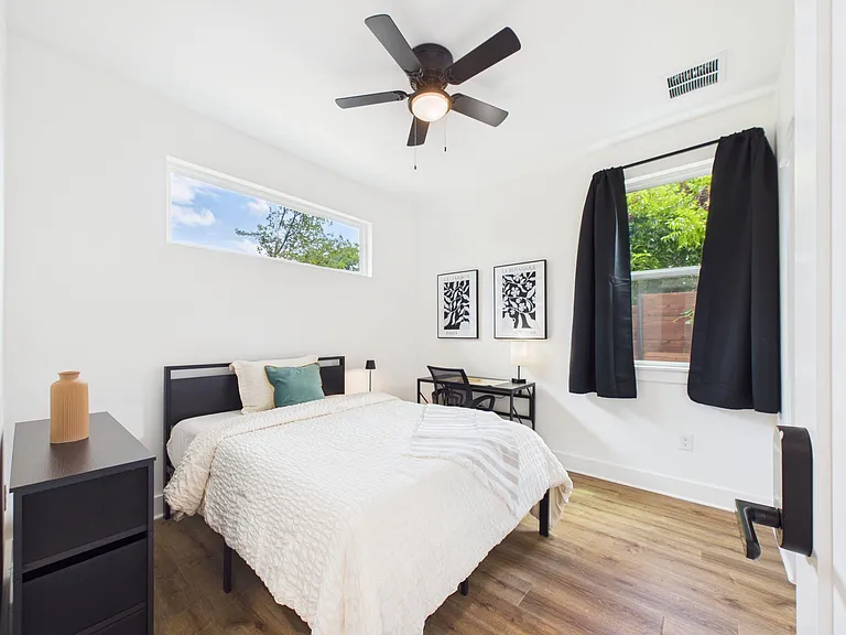Private bedroom with ceiling fan, wide windows, and wood-style flooring, plus a dedicated desk area for work or study.