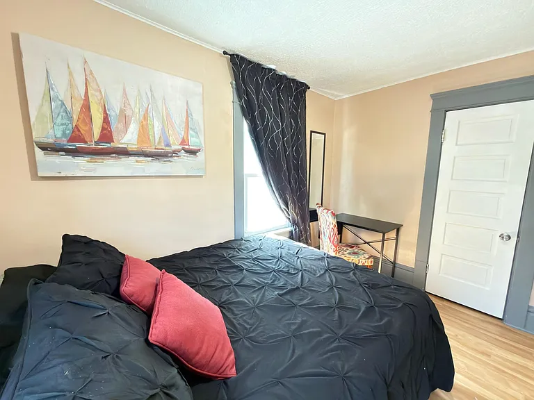 Furnished bedroom with a full bed, window with curtains, wall art, and a small desk setup for work or study.