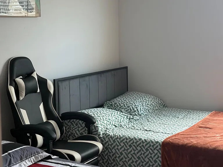 Furnished bedroom with two beds, a comfortable chair, and a window with blinds for light and privacy.