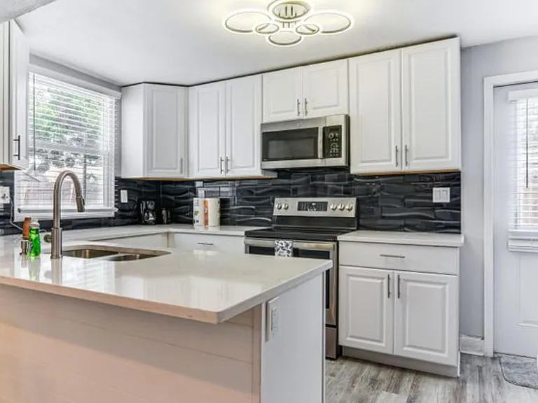 Updated kitchen with ample white cabinetry, stainless-steel appliances, and a large island with double sink for prep space.