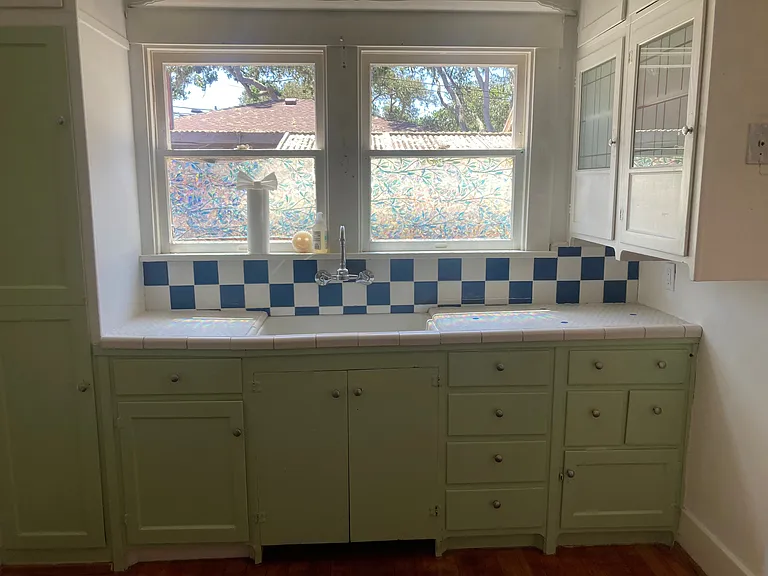 A charming kitchen with period tile and cabinets, an original cooler, and much storage.