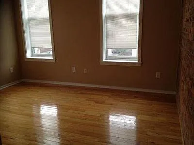 Empty larger bedroom facing the front of Kenwood Ave with brick wall on the right.