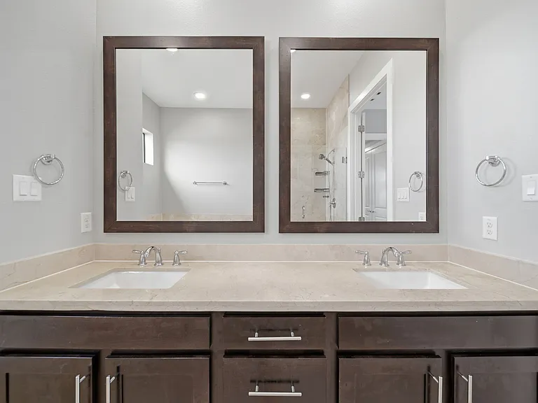 Modern bathroom featuring a dual-sink vanity with sleek natural stone countertops and rich dark wood cabinetry. Oversized framed mirrors enhance the sense of space, while soft neutral gray tones create a clean, spa-like atmosphere.