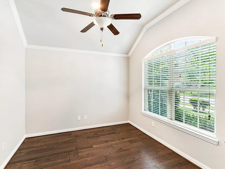 Vaulted ceiling room featuring a large arched window with blinds, wood-finish flooring, and a ceiling fan