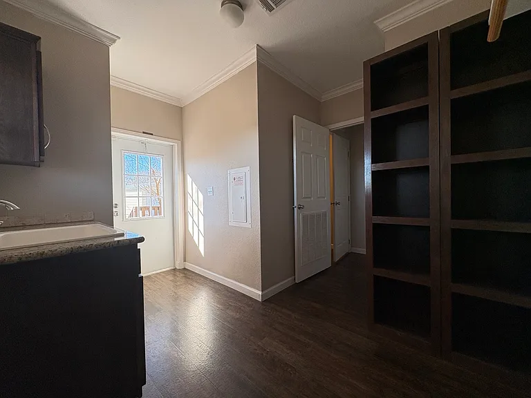 laundry room with door heading out to garage. laundry sink on left and shelves on right. other door leads to bedroom 2 and rest of house.