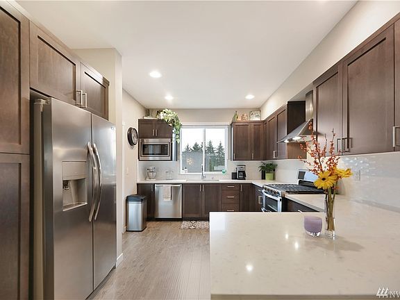 This kitchen features stainless steel appliances, hood vent, backsplash and quartz counter tops.