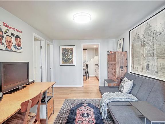 Living room area with desk, TV, couch, and view into the kitchen.
