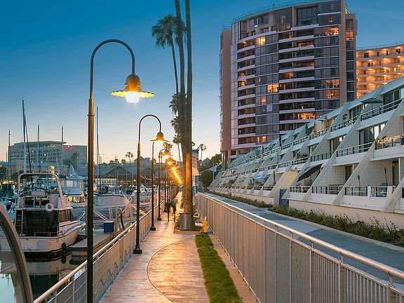 Walkway lit with lamps next to apartment building and marina with boats.