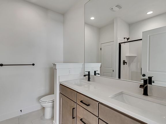 Modern bathroom with a double vanity, black fixtures, large mirror, and light-colored walls. Toilet