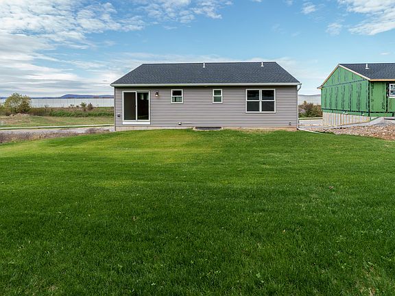 Rear view of home showing gray siding, sliding glass door, and large grassy backyard under blue sky.