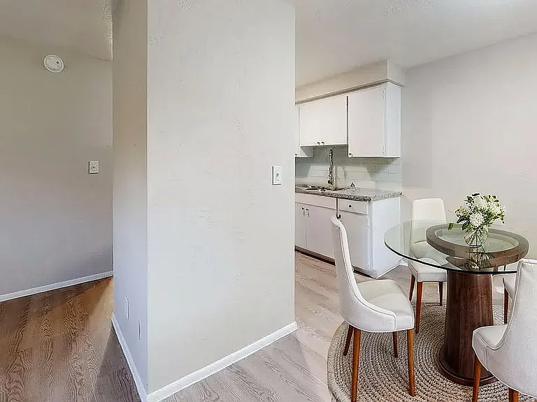 Modern apartment dining area with elegant glass table and white chairs, adjacent to a sleek, contemporary kitchen.