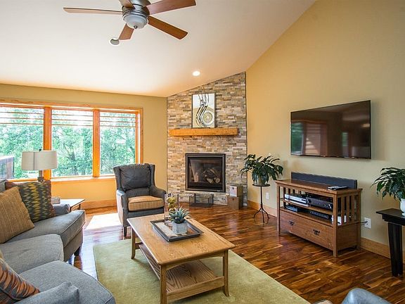 Great room includes a vaulted ceiling, gas fireplace with Sunset Gold dry-stacked stone, Kichler ceiling fan, and Jeldwen Wood Casement windows with custom grills overlooking scenic back yard.