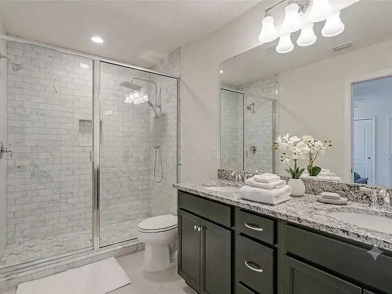 Spacious bathroom with a double-sink granite vanity, large mirror, and glass-enclosed shower with tile surround.