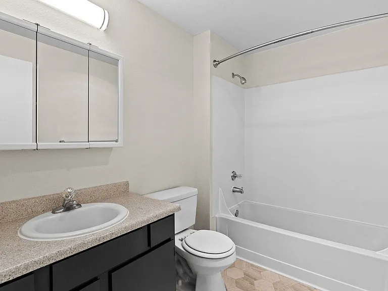 Full bathroom with dark vanity cabinetry, granite-style countertop, mirrored medicine cabinet, and tub/shower combo at Garden Square Apartments in Lakewood, WA. Full bathroom with dark vanity cabinetry, granite-style countertop, mirrored medicine cabinet,