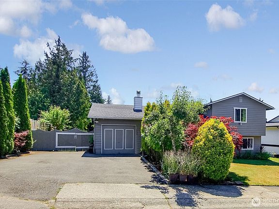 Detached garage with extended driveway, surrounded by mature landscaping and evergreens.