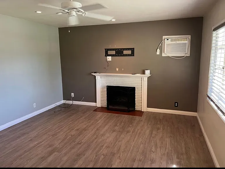 Living room with wood burning fireplace, ceiling fan and wall ac unit.
