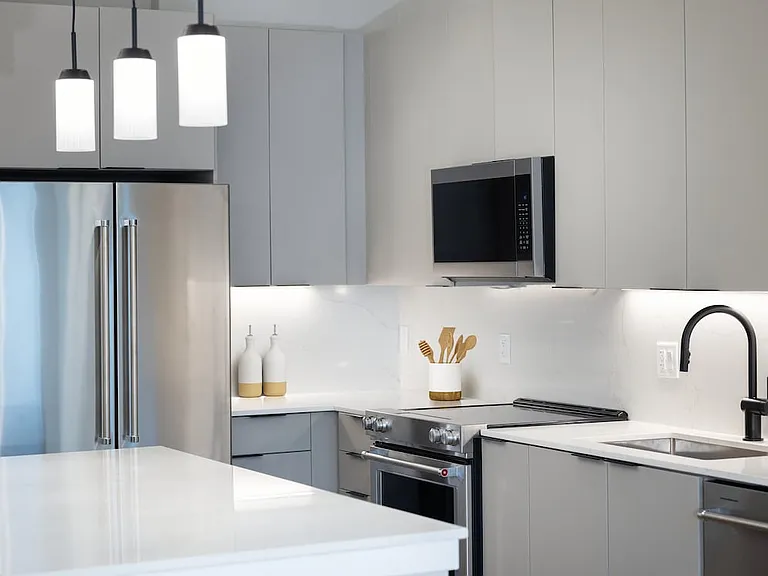 Signature Collection kitchen with stainless steel appliances, light grey cabinetry, marbled quartz countertops and backsplash, under-cabinet lighting, and pendant lighting