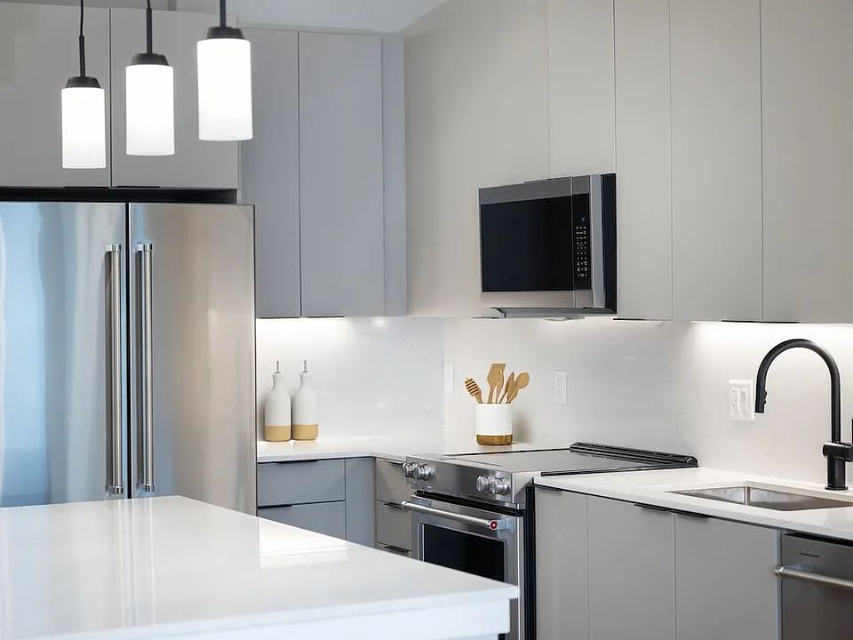 Signature Collection kitchen with stainless steel appliances, light grey cabinetry, marbled quartz countertops and backsplash, under-cabinet lighting, and pendant lighting