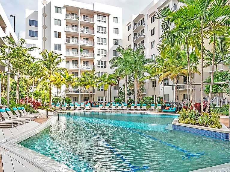 Luxury apartment resort-style pool with palm trees, sun loungers, and landscaped courtyard