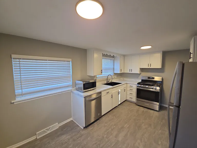 Bright kitchen with updated countertops, white cabinetry, stainless refrigerator and range, and dishwasher.