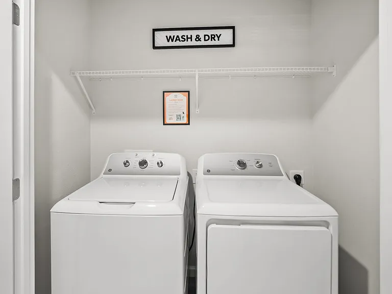 Dedicated laundry closet with full-size washer and dryer plus an overhead wire shelf for convenient storage.